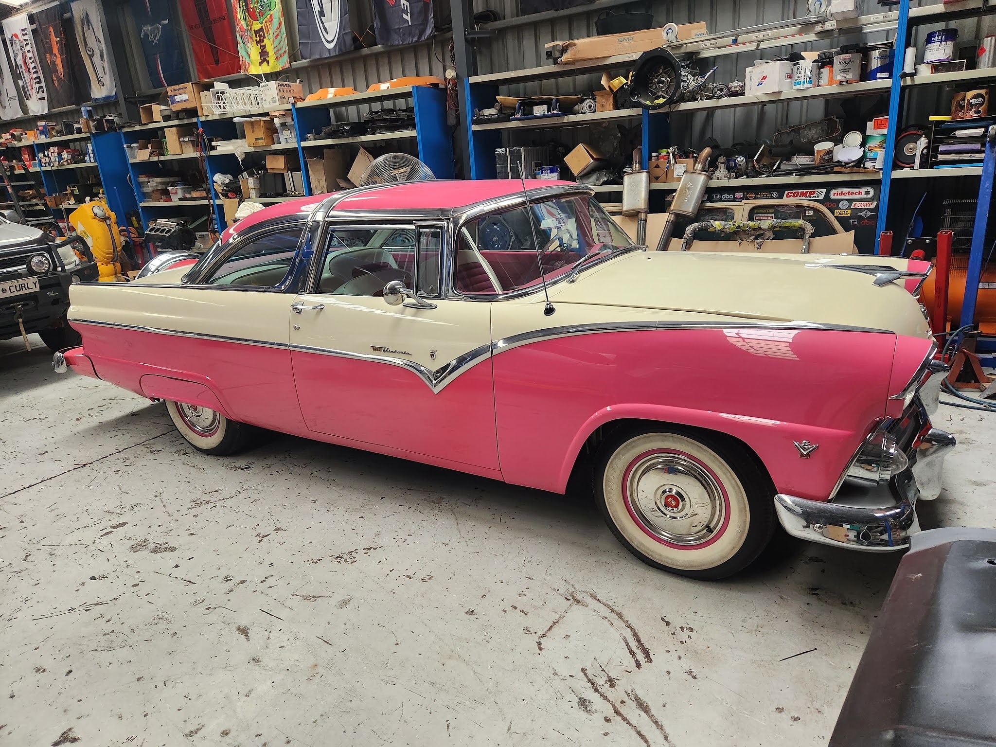 A Ford Crown Victoria in hot pink and cream with chrome trim and whitewall tyres inside the workshop