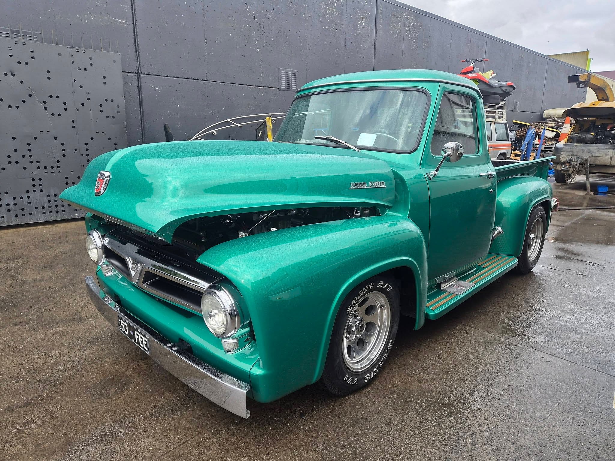 A Ford F100 pickup in deep teal, front three quarter, with a chrome grille and bumper