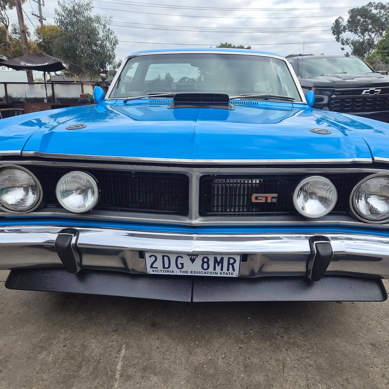 The front of a blue Ford Falcon GT showing quad headlights, the GT grille badge and a front spoiler