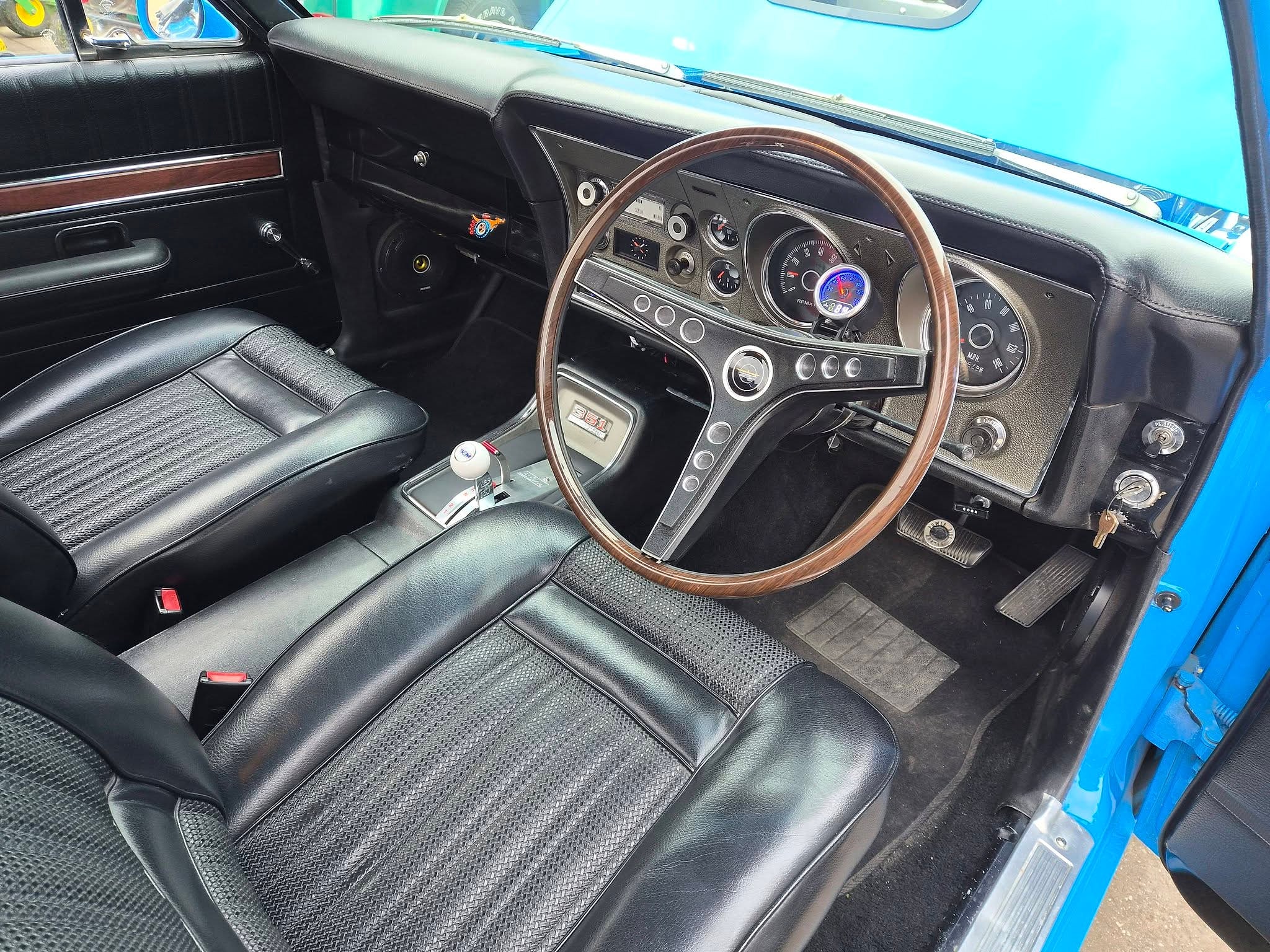 The interior of a Falcon GT with black vinyl bucket seats, a wood rim steering wheel and the original gauges