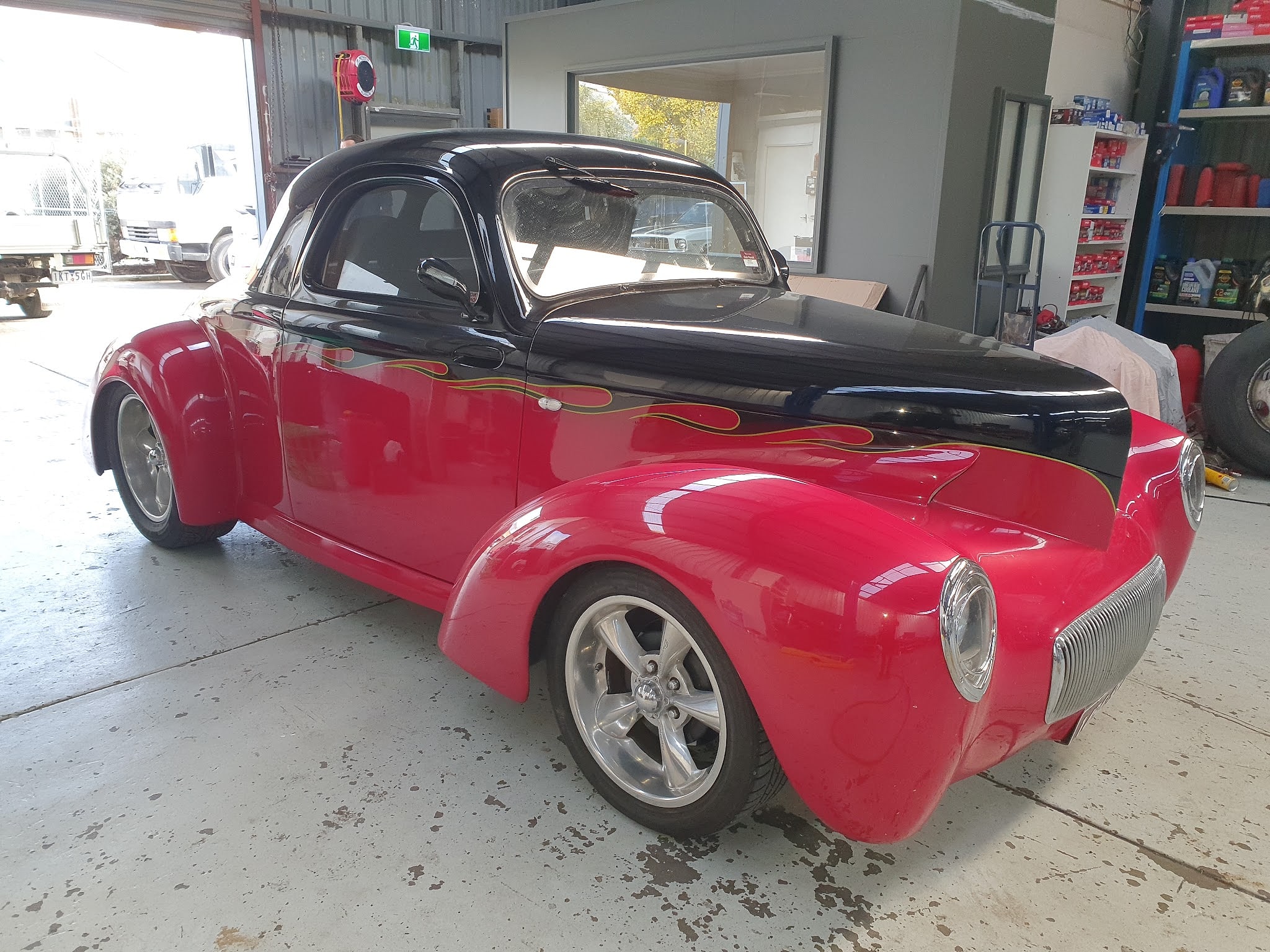 A Willys coupe in red with a black bonnet and roof and yellow edged flames along the side, in the roller door